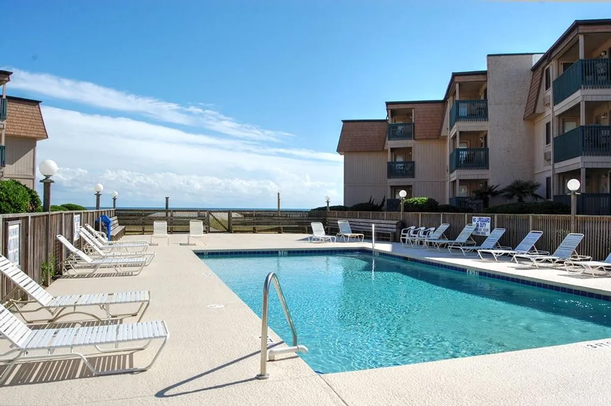 This image features a vibrant swimming pool with lounge chairs strategically placed nearby, all set against a backdrop of sweeping ocean views. The scene is lively and inviting, suggesting opportunities for swimming, sunbathing, and family relaxation just steps from the beach.