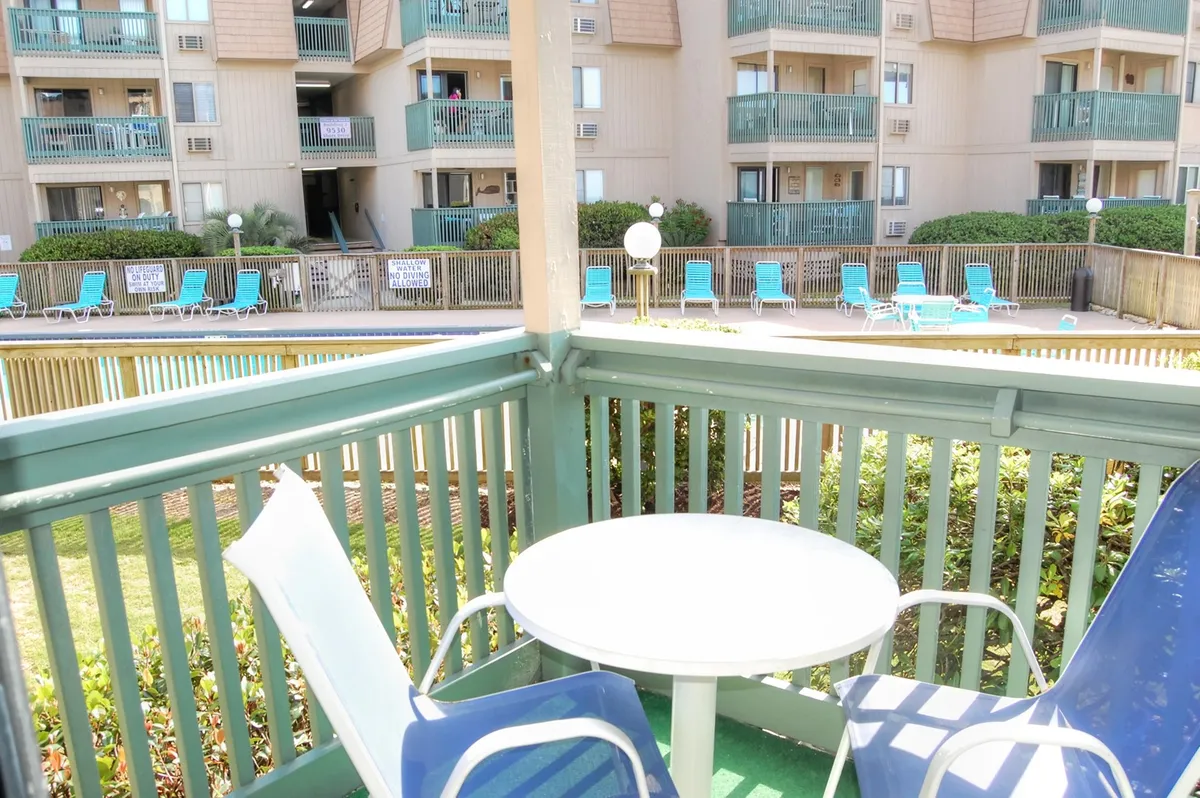 This image captures an inviting outdoor seating area overlooking a swimming pool, with a private balcony view in the background. The scene naturally evokes morning coffee moments or evening relaxation, blending the serenity of the pool with glimpses of the ocean horizon.