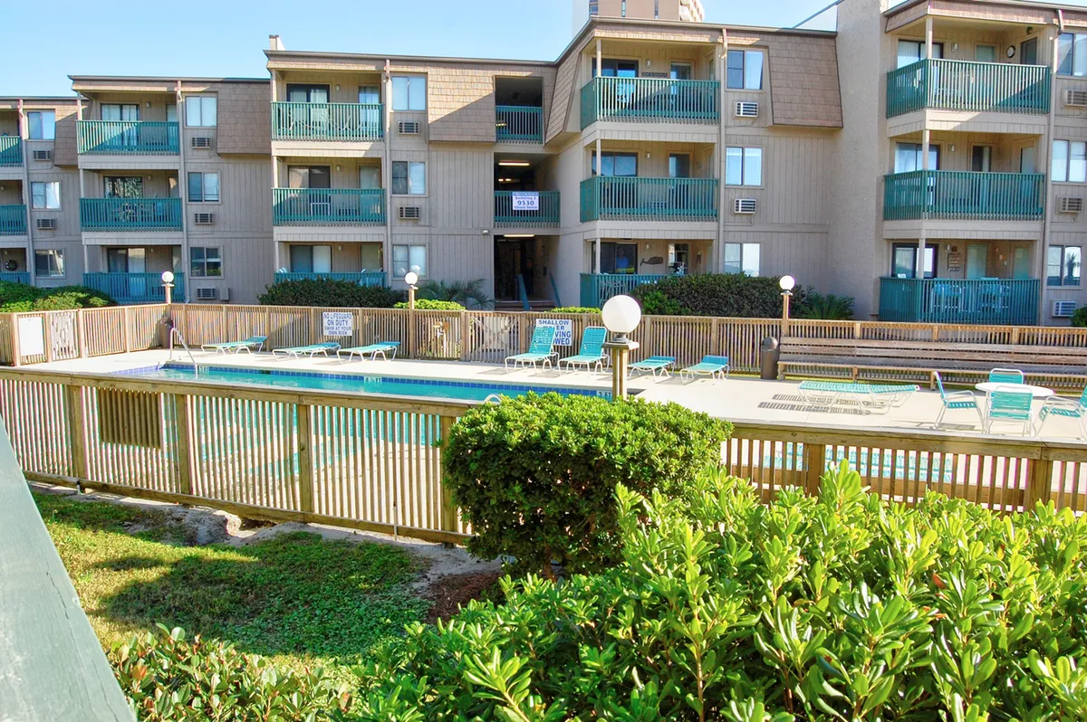 This image shows a resort swimming pool surrounded by balconies, with green shrubbery adding a touch of nature. The scene is bright and cheerful, with a relaxed atmosphere that invites residents and guests to swim, sunbathe, and socialize by the water.