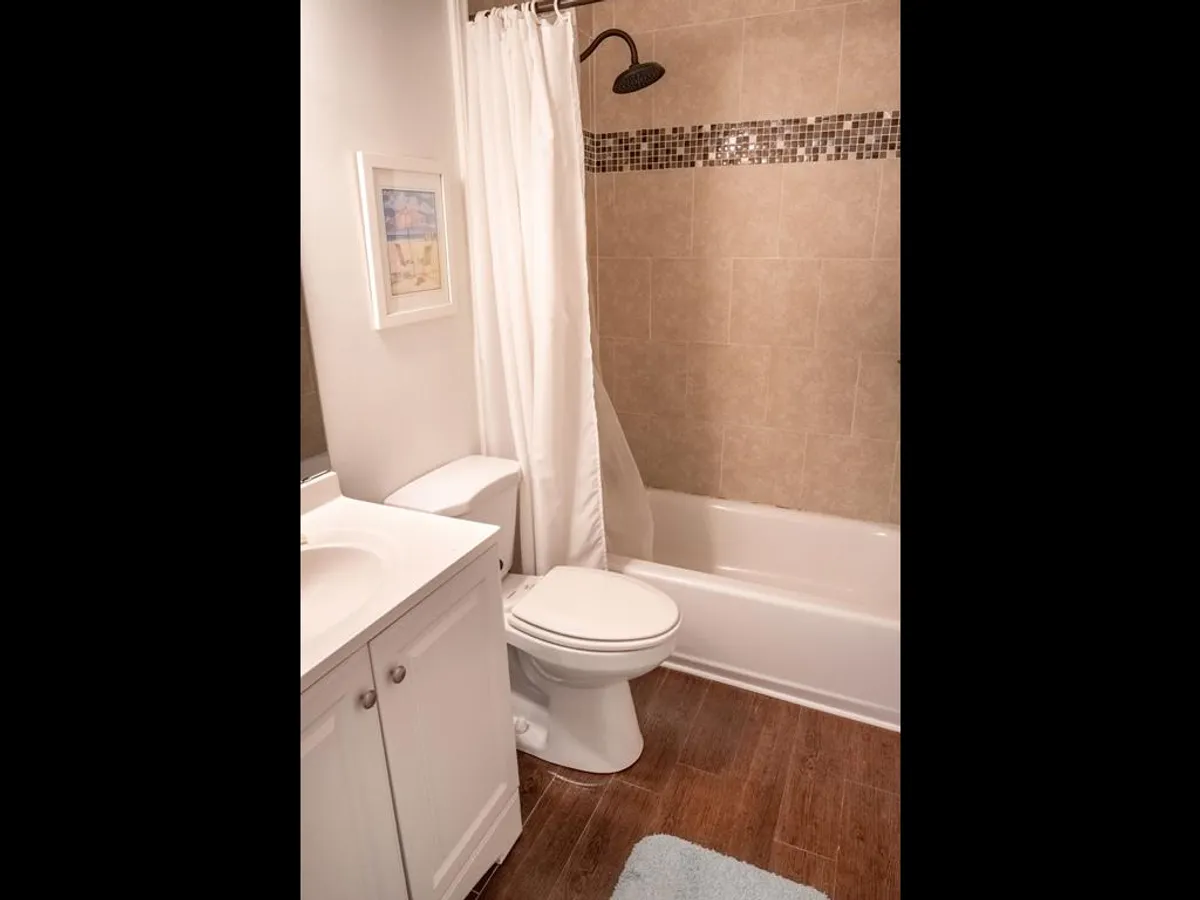 An inviting interior bathroom with a bathtub, vanity, shower curtain, and toilet, complemented by tasteful framed artwork. The space is well-lit and serene, offering an ideal spot for unwinding after a day of adventure.